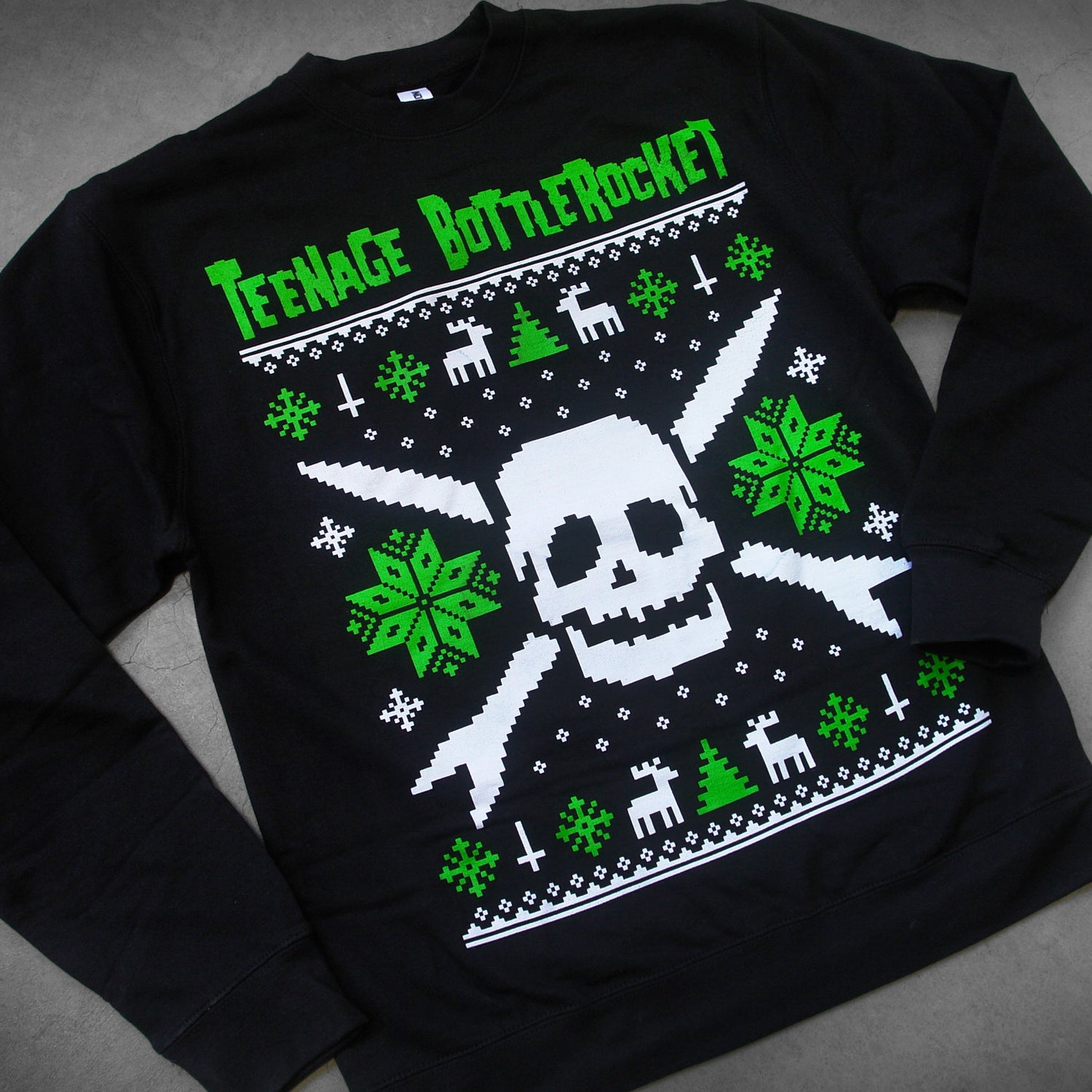 close up, angled image of a black crewneck sweatshirt laid flat on a concrete floor. crewneck has a skull in the center with snow flakes, reindeer and trees surrounding it in the style of a Christmas sweater. at the top says teenage bottlerocket