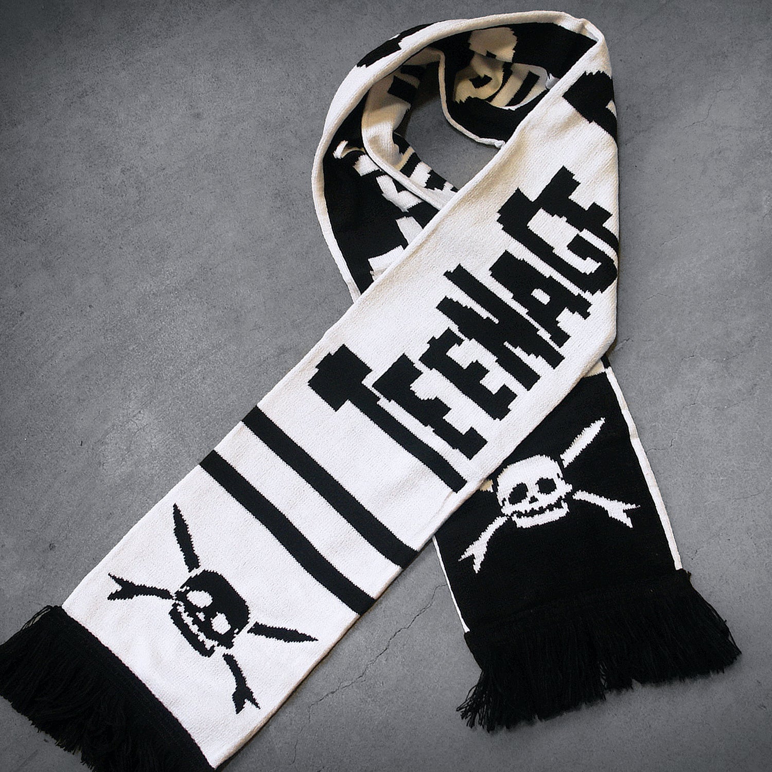 image of a wrapped up custom scarf laid on a concrete floor. the scarf is white with black text that says teenage bottle rocket and has black skulls by each fringed edge