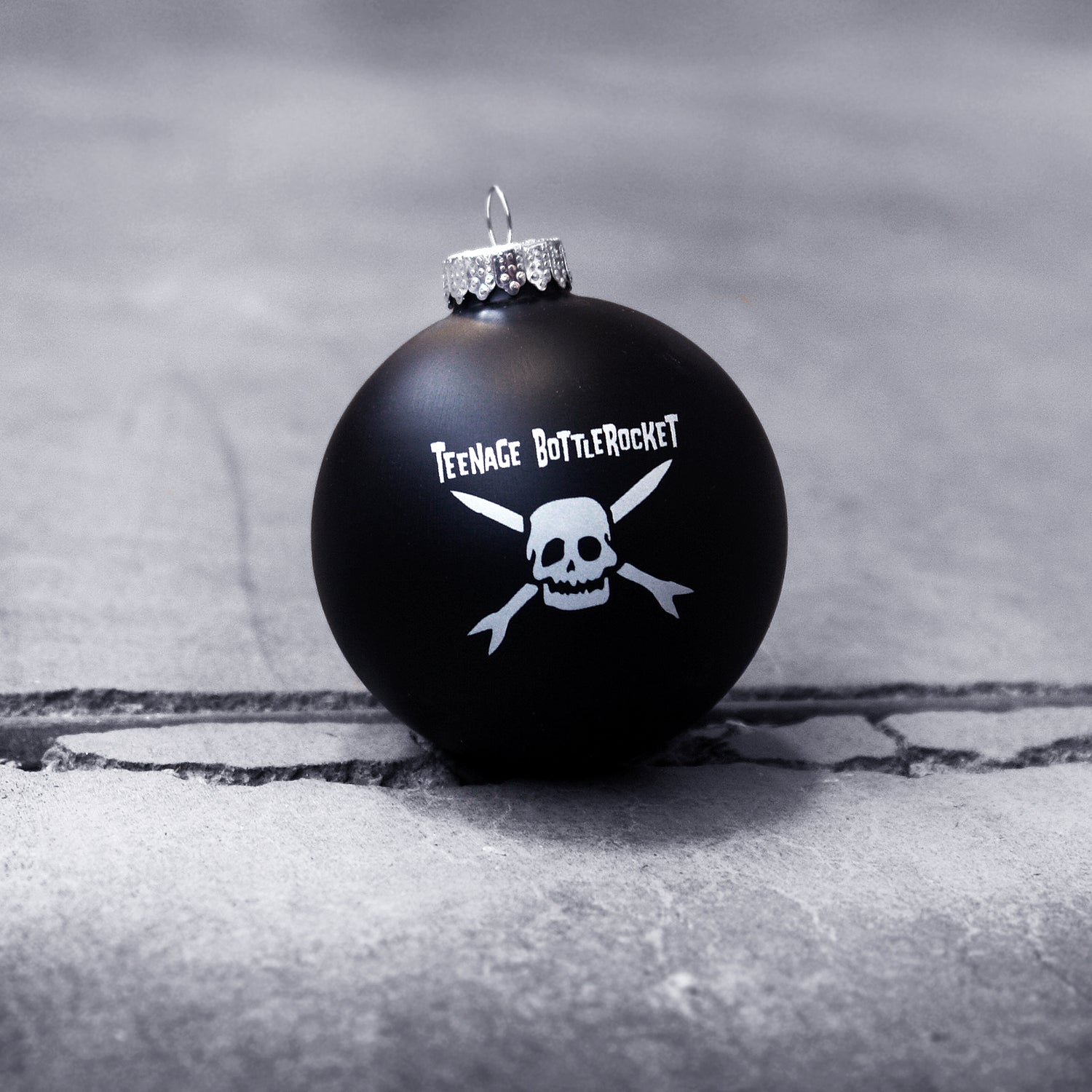 image of a black ball christmas ornament on a cracked, concrete floor. ornament has white print of a skull and the words teenage bottlerocket at the top.